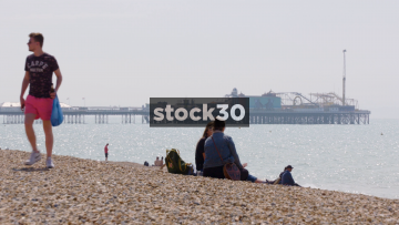 People Sitting On Brighton Beach, Brighton Palace Pier In Background, UK